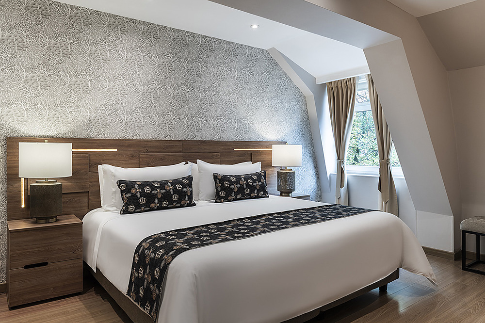 Elegante habitación de hotel con cama grande, cabecero de madera, papel tapiz decorativo y lámparas de noche. Porton de la Cabrera