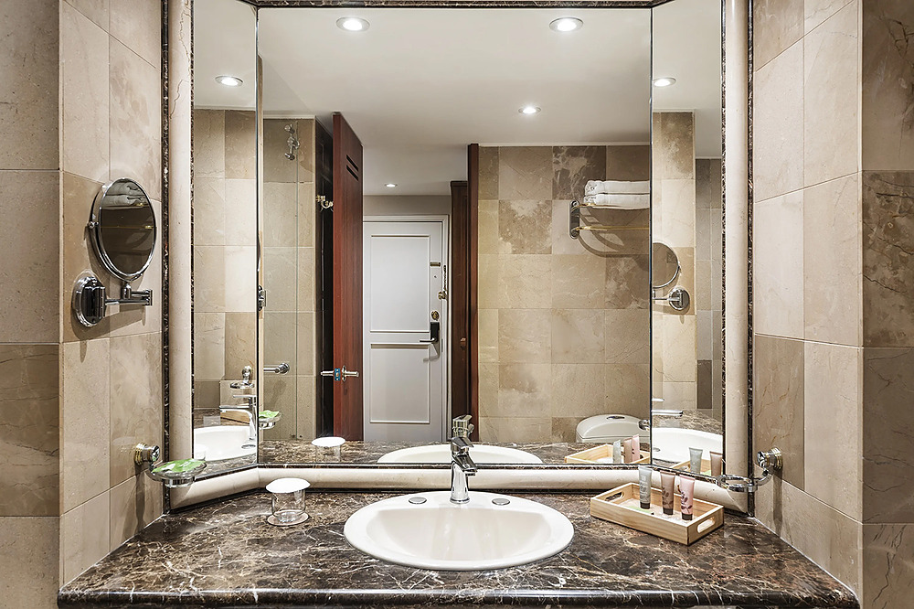 Baño de hotel con lavabo, espejo y amenidades. Porton de la Cabrera