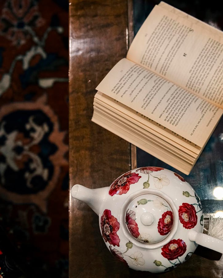 Tetera floral y libro abierto sobre mesa de madera, perfecto para una estancia Porton de la Cabrera.