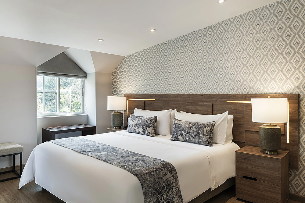 Habitación de hotel con cama king, ropa de cama blanca yPorton de la Cabrera decorativa.