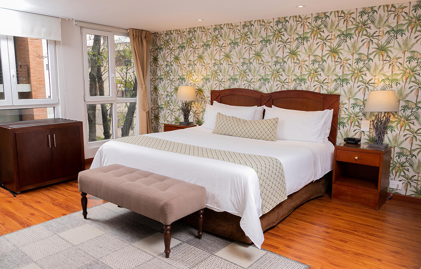 Dormitorio con papel tapiz de palmeras, cama king, mesita de noche y banco. Porton de la Cabrera