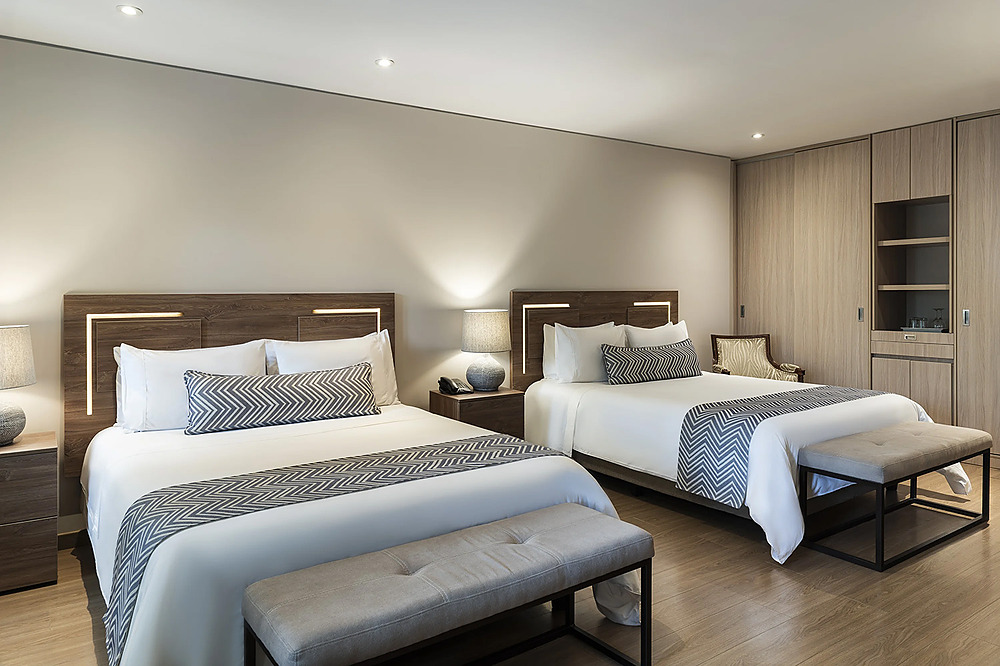 Habitación de hotel con dos camas, ropa de cama blanca, almohadas decorativas y Porton de la Cabrera.