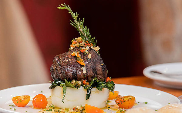 Filete de res conPorton de la Cabrerapuré de patatas y tomates cherry en plato blanco.