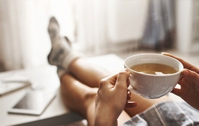una mujer está sentada en el suelo con las piernas cruzadas y sosteniendo una taza de café .