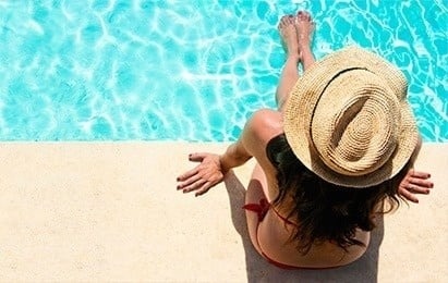 a woman in a hat sits on the edge of a swimming pool