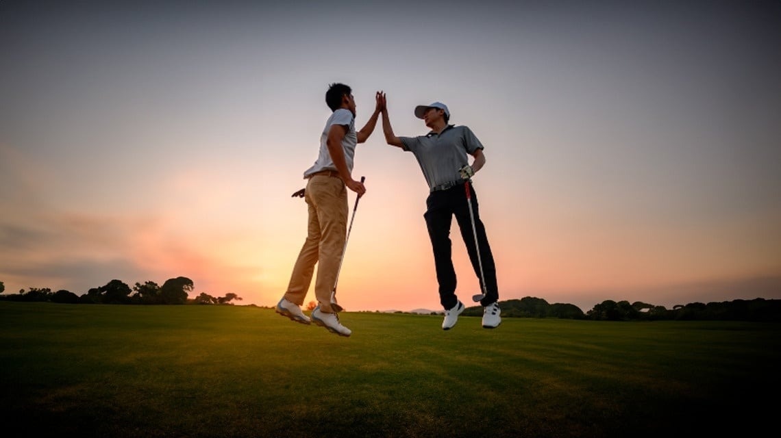 deux golfeurs se donnent un high five sur un terrain de golf au coucher du soleil