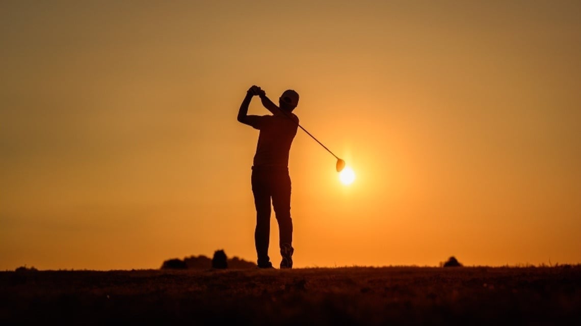 un homme joue au golf au coucher du soleil