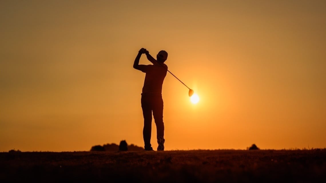 un hombre golpea una pelota de golf al atardecer