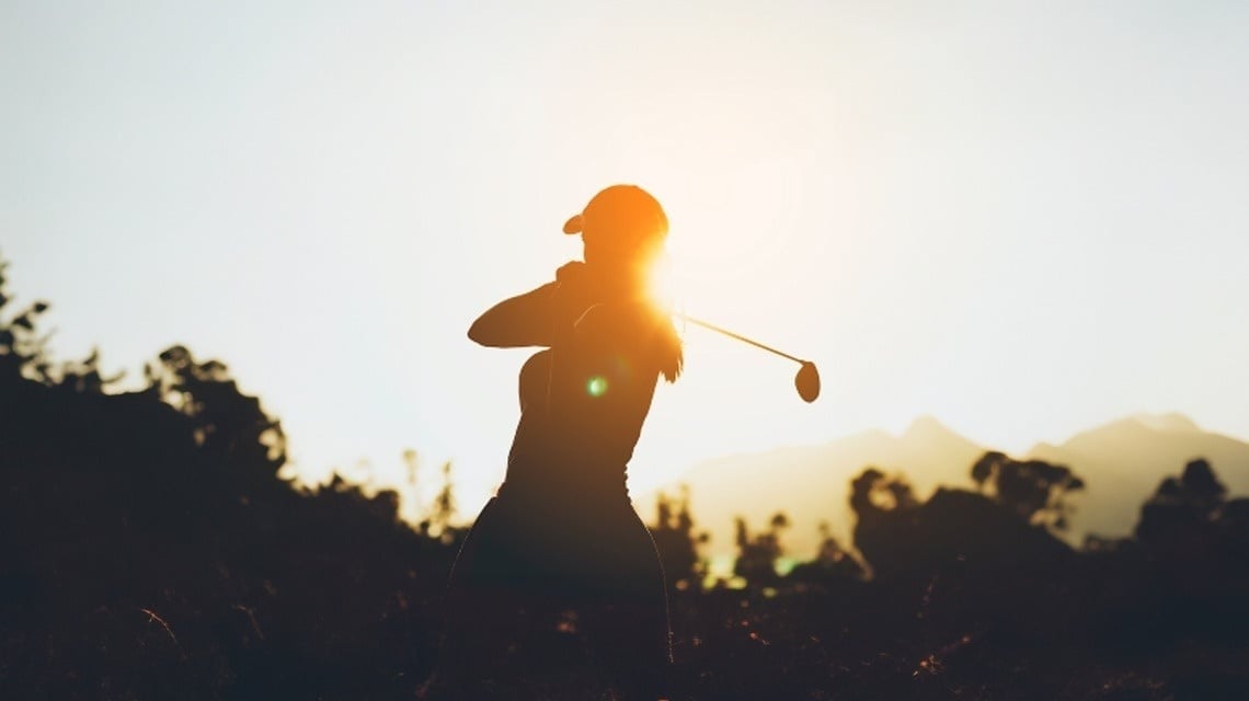 a silhouette of a woman swinging a golf club at sunset