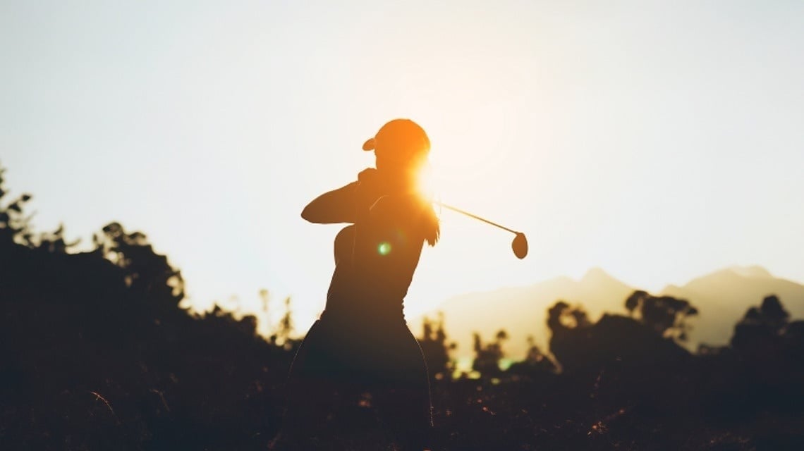 una mujer golpea una pelota de golf al atardecer