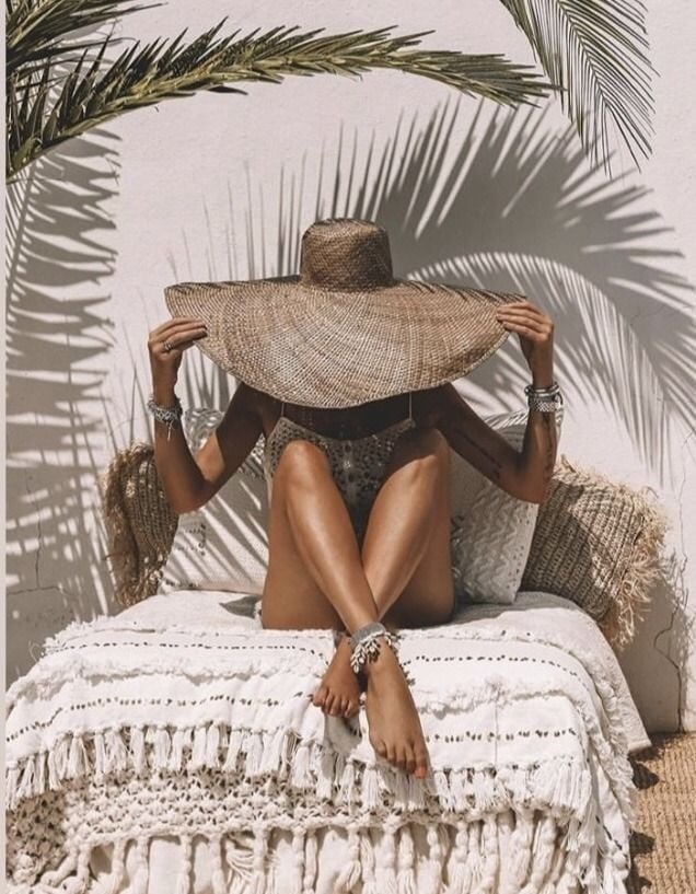 a woman wearing a straw hat sits on a bed