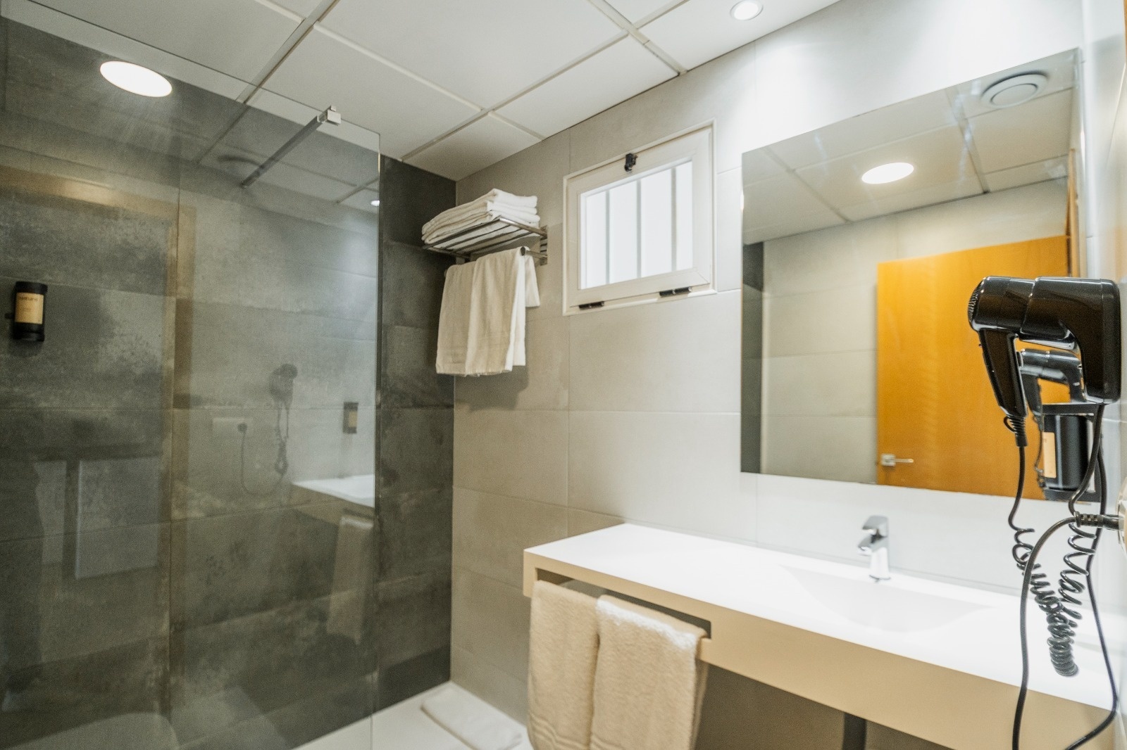 Baño moderno en Primavera Loix Apartamentos con ducha, secador y toallas.