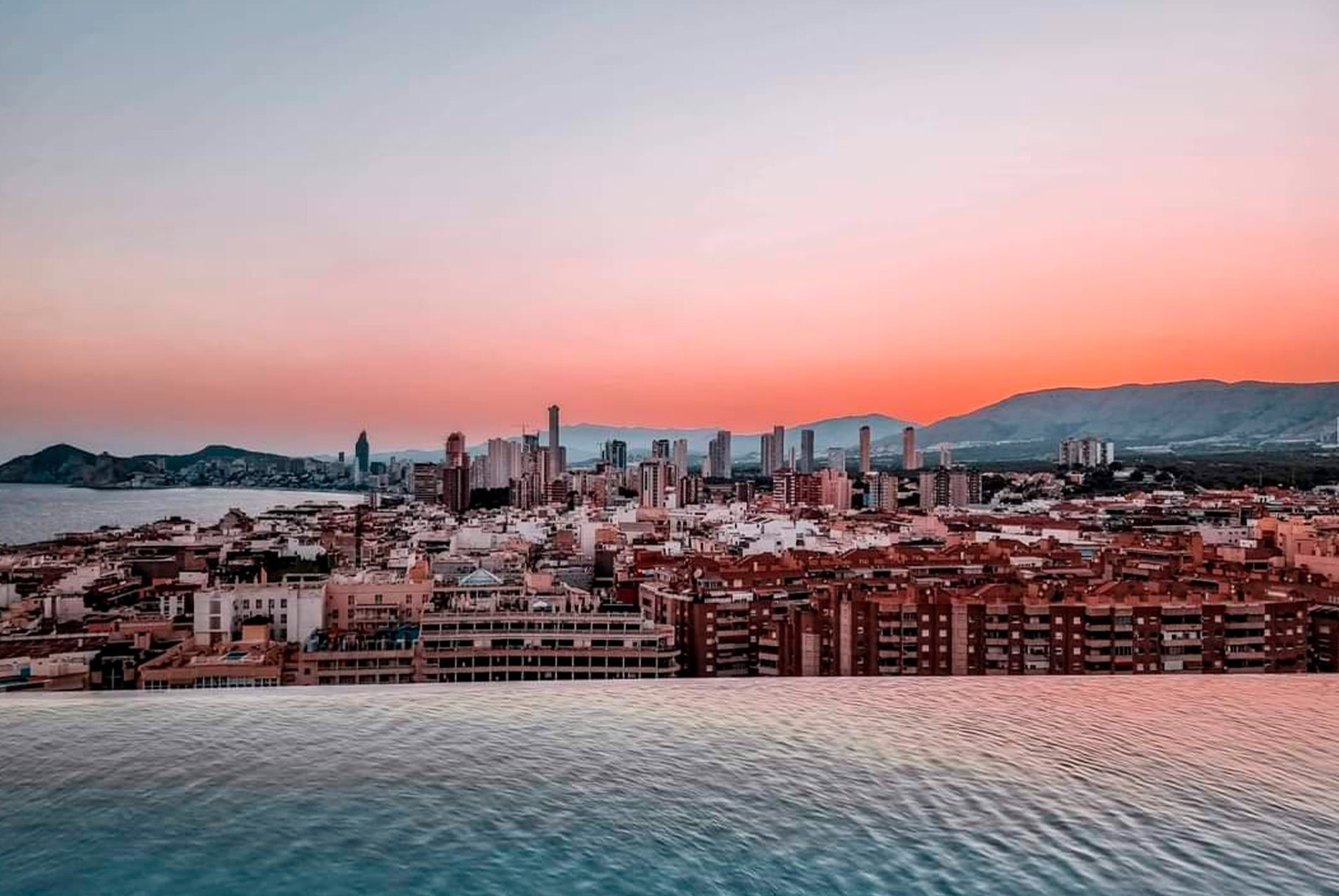 a view of a city from an infinity pool at sunset