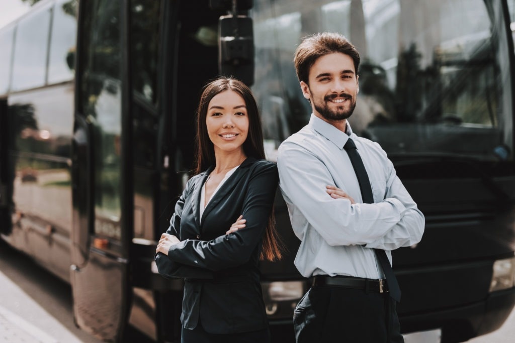 a man and a woman standing in front of a bus with their arms crossed