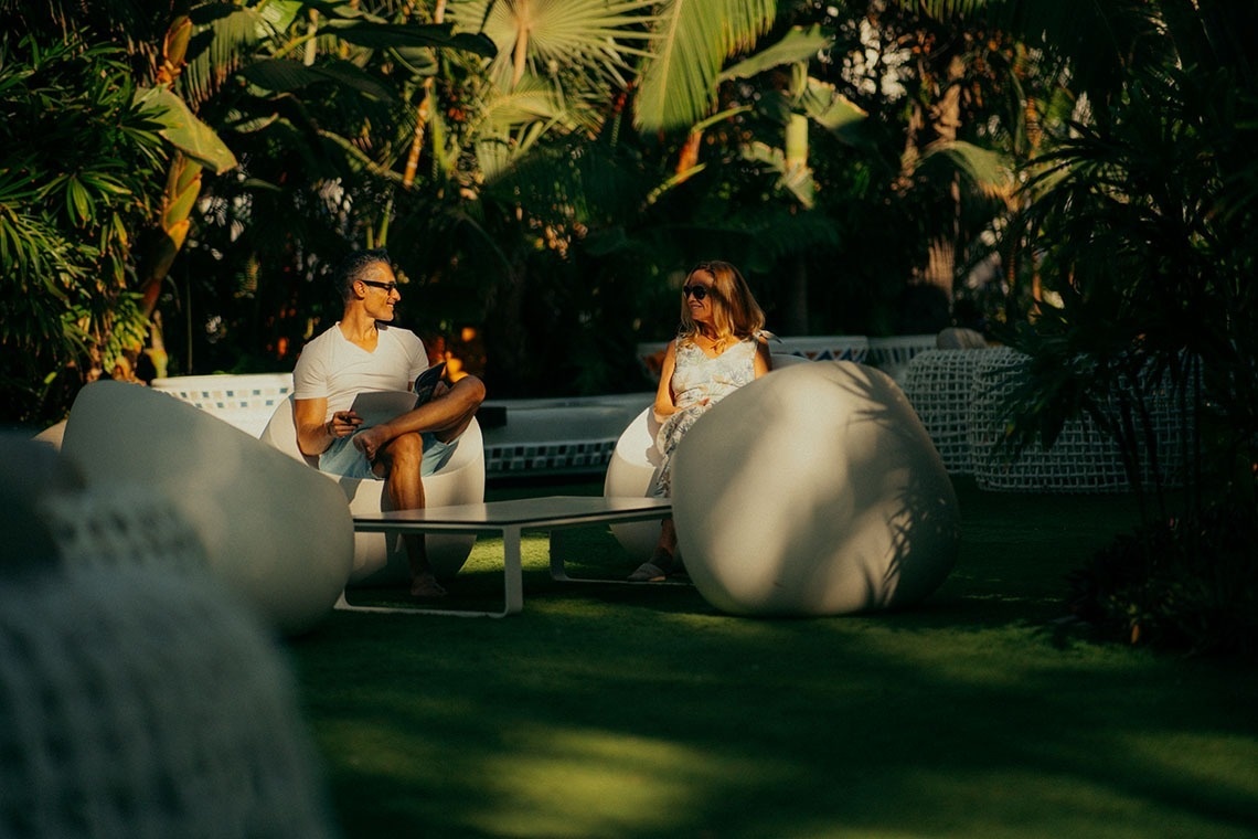 a man and a woman sit in white chairs in a garden