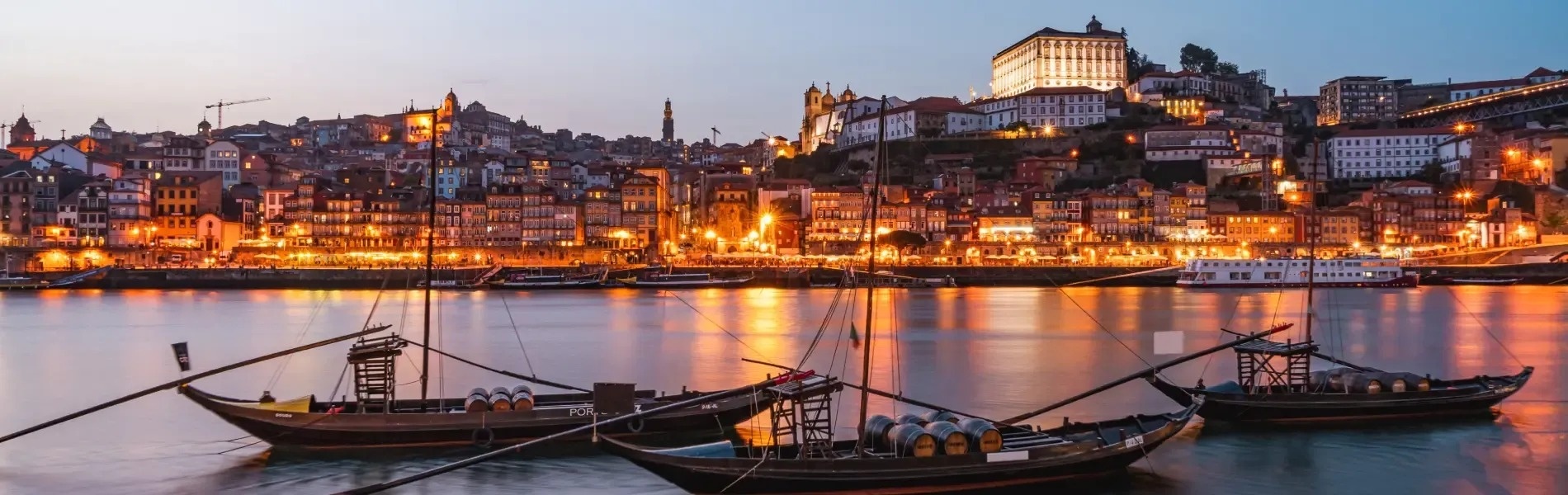 um grupo de barcos está ancorado em um rio com uma cidade ao fundo