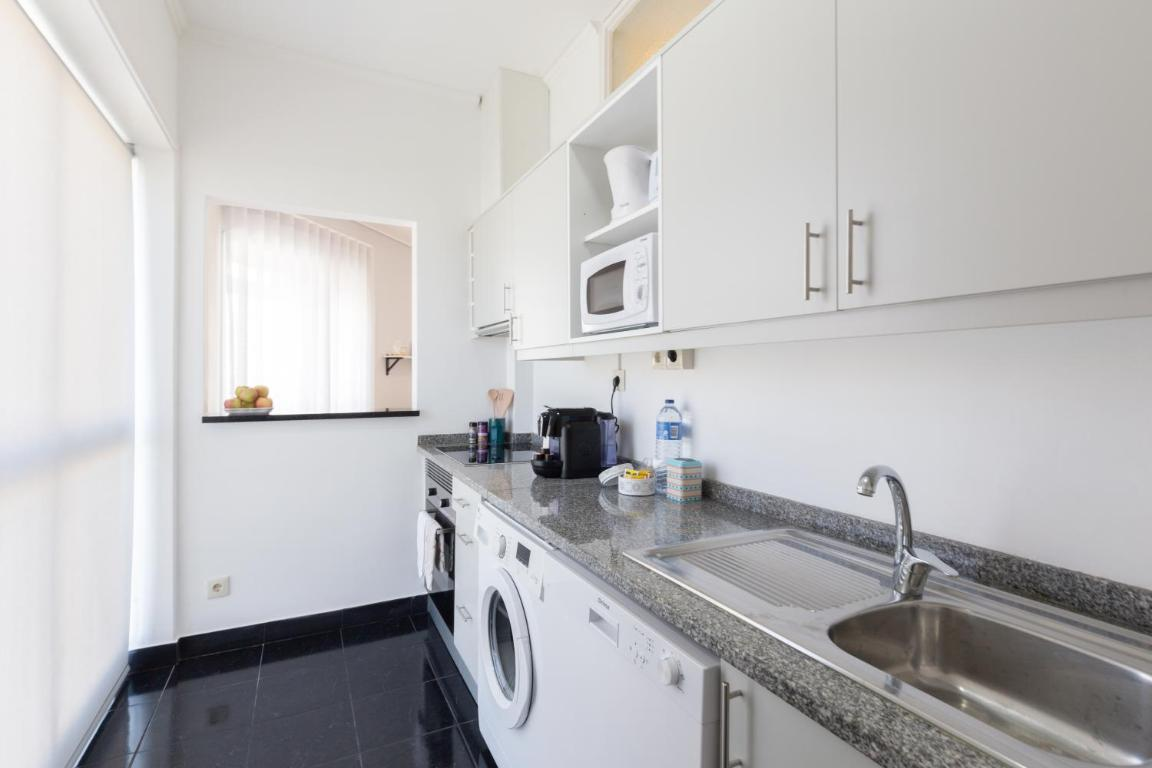 uma cozinha com armários brancos e pia de aço inoxidável