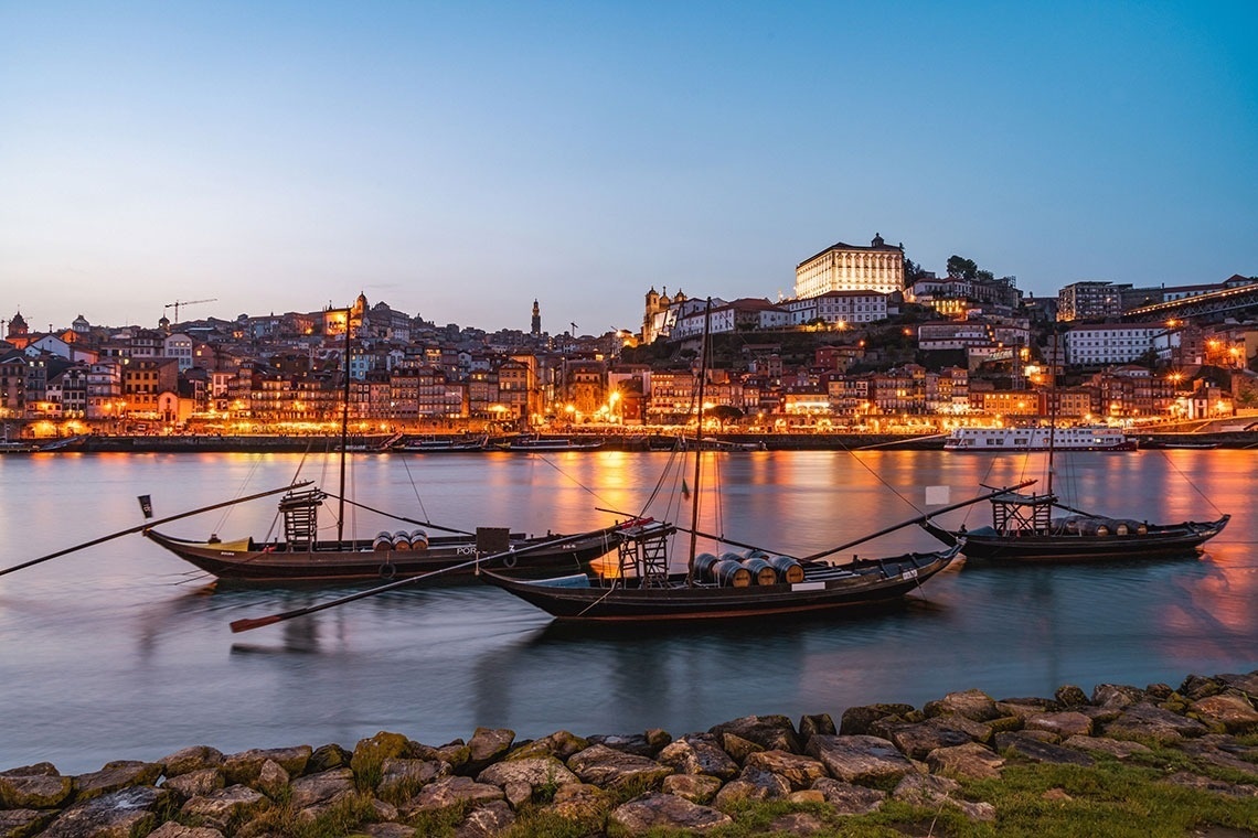 a row of boats in the water with a city in the background