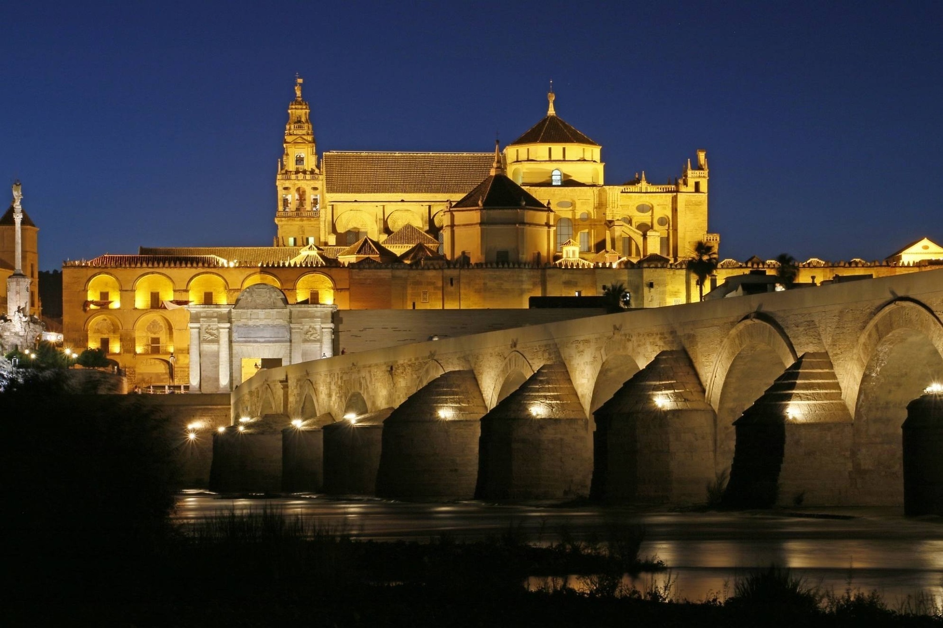 una catedral iluminada por la noche con un puente en primer plano