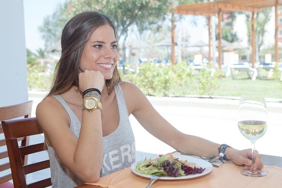 una mujer se sienta en una mesa con un plato de ensalada y un vaso de vino