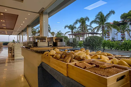 Desayuno buffet en Hotel Puerto Bahía Spa con frutas, pan y bebidas. Vista al exterior.
