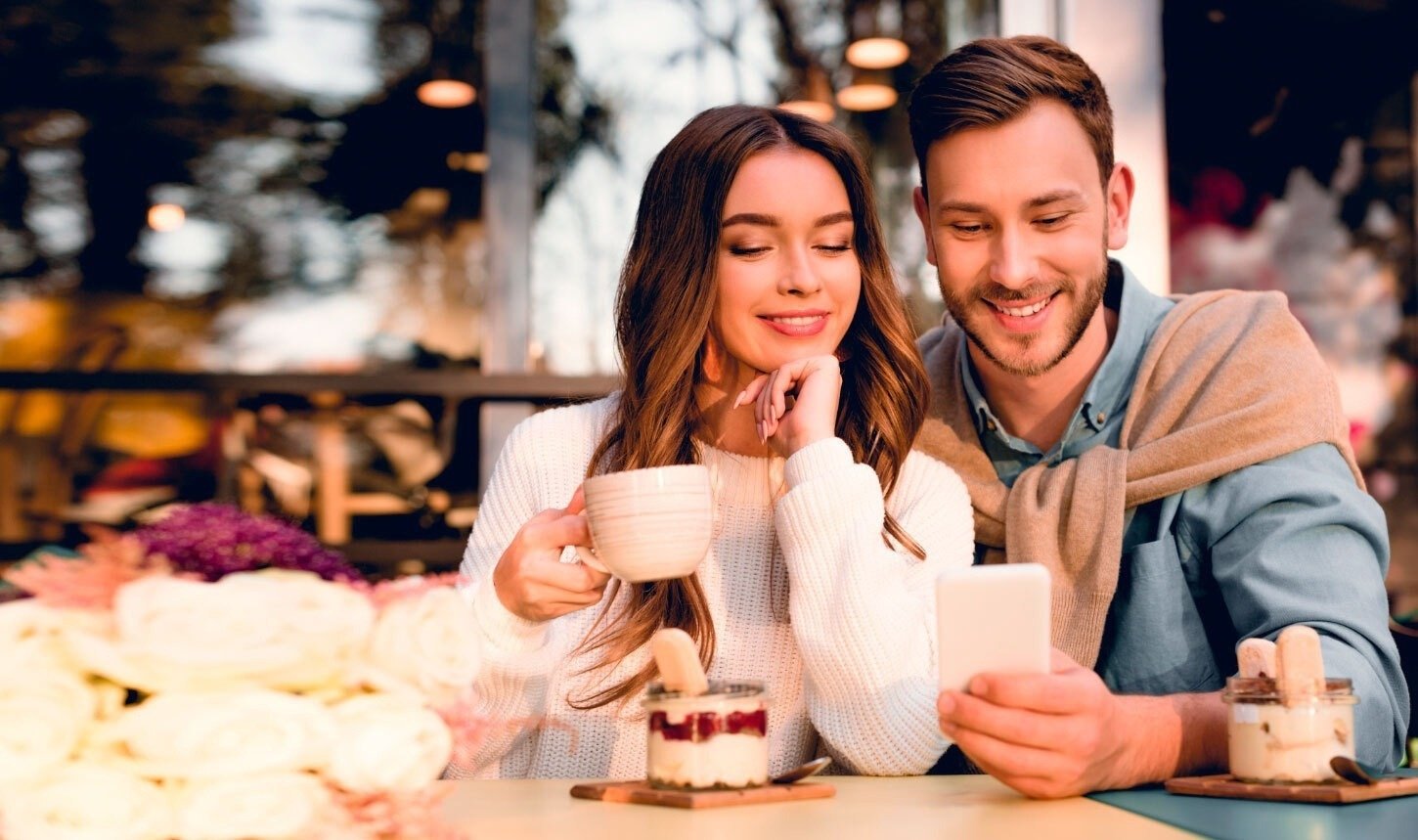 un hombre y una mujer miran un teléfono inteligente mientras sostienen tazas de café