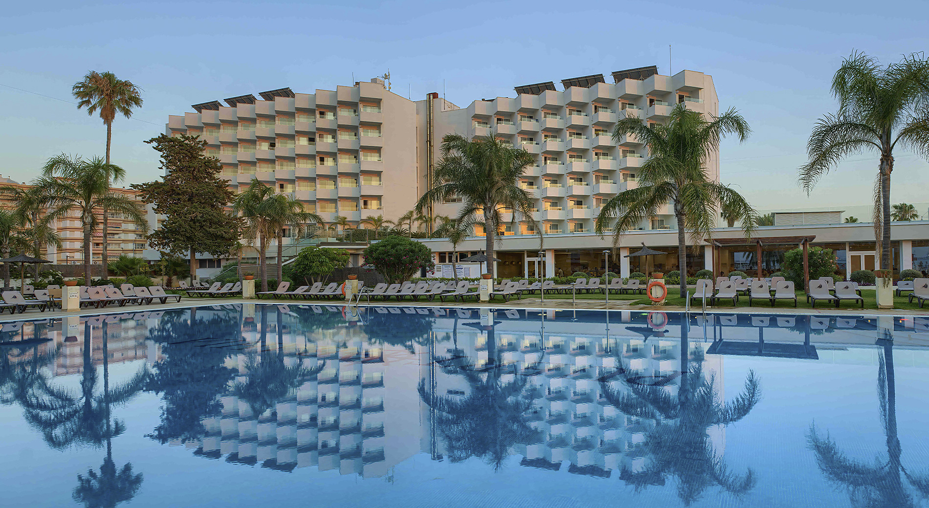 Galería de imágenes Hotel Puertobahía: piscina y edificios al atardecer.