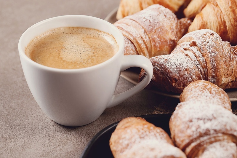 una taza de café junto a un plato de croissants cubiertos de azúcar en polvo