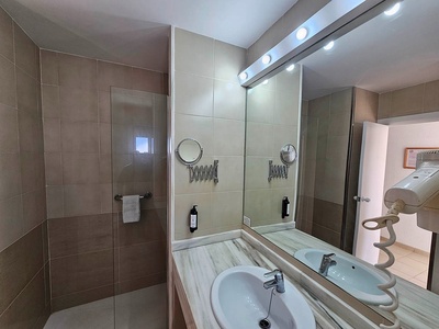 Un moderno baño con un lavabo, un espejo iluminado, una ducha con mampara de cristal y un secador de pelo colgado en la pared.