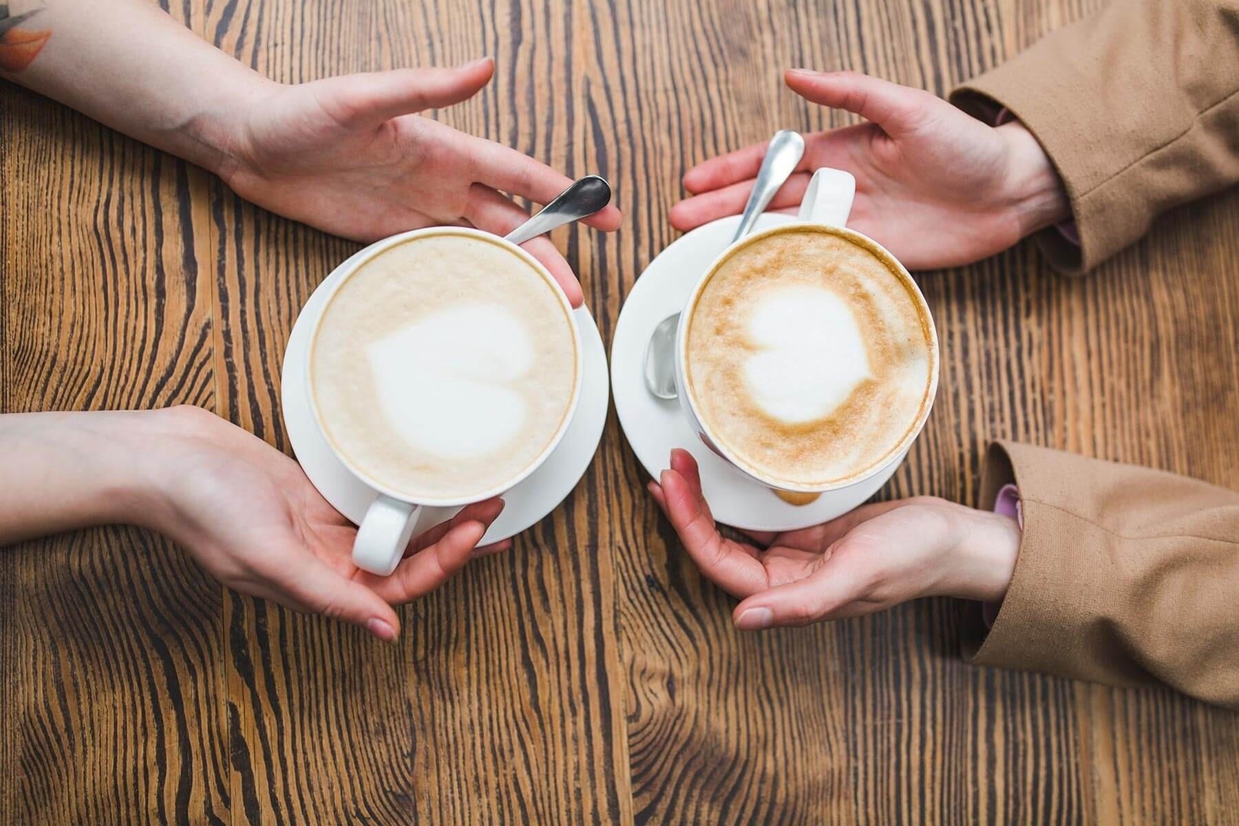 two people holding cups of coffee with a heart shaped foam