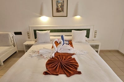 Una cama de hotel está decorada con toallas blancas formando cisnes y una manta terracota plegada.