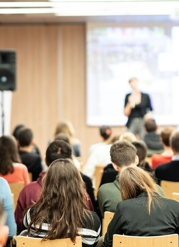 a group of people are sitting in a lecture hall watching a presentation .