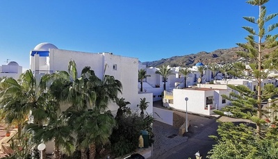 a row of white buildings with palm trees and mountains in the background
