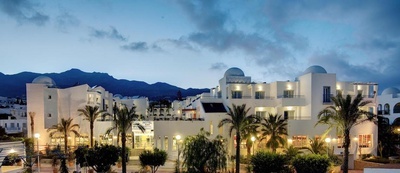 un hotel blanco con palmeras y montañas en el fondo - 