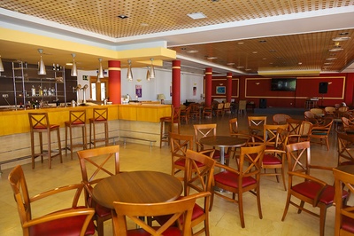 Bar y salón del Hotel El Puntazo con mesas de madera y sillas rojas. - 