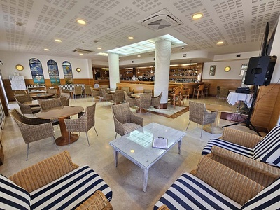 Interior de un acogedor salón o bar con mobiliario de mimbre, decoración náutica que incluye vitrales marinos, una barra y equipo de sonido. - 