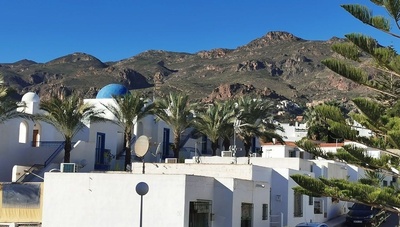 un edificio blanco con una cúpula azul está rodeado de palmeras y montañas