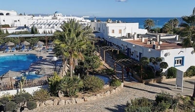 una piscina rodeada de palmeras y edificios blancos con el océano al fondo