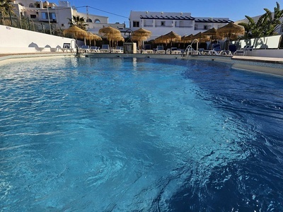 una piscina rodeada de sillas y sombrillas y un edificio blanco - 