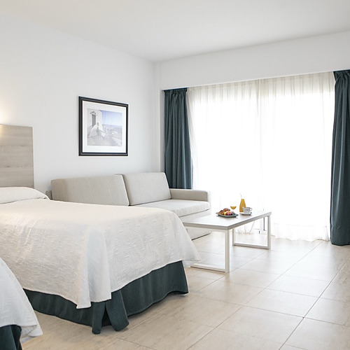 Habitación luminosa con dos camas, sofá, mesa y cocina. PYR Fuengirola ideal para familias.