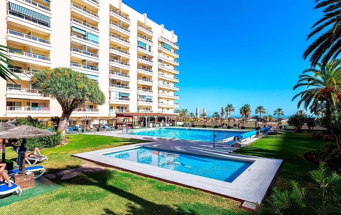 una piscina rodeada de césped y palmeras frente a un edificio de apartamentos