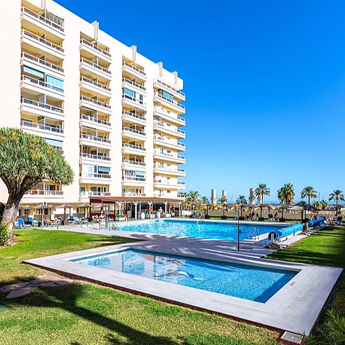 Edificio de apartamentos con piscina y palmeras, ideal para tu PYR Fuengirola.