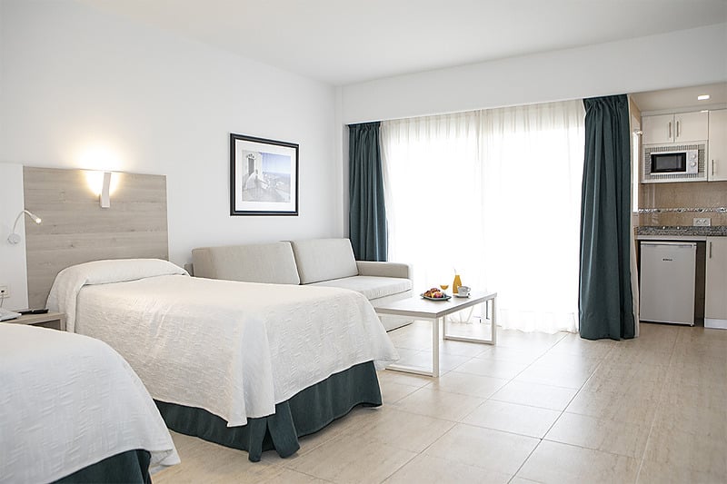 Chambre d'hôtel lumineuse avec deux lits, un coin salon et une kitchenette, parfaite pour votre séjour PYR Fuengirola.