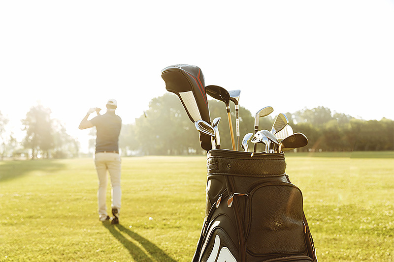Sac de golf avec un joueur en arrière-plan sur un terrain de golf baigné de soleil pour votre séjour PYR Fuengirola.