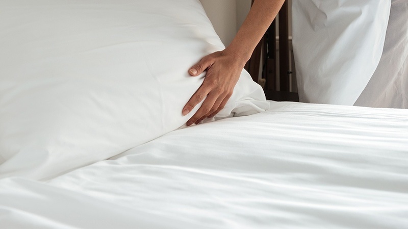 PYR Fuengirola : Main ajustant un oreiller sur un lit d'hôtel blanc immaculé.
