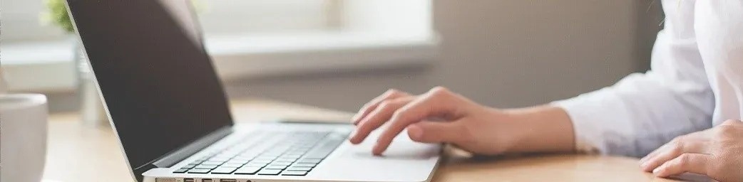 een persoon typt op een laptopcomputer op een houten tafel .