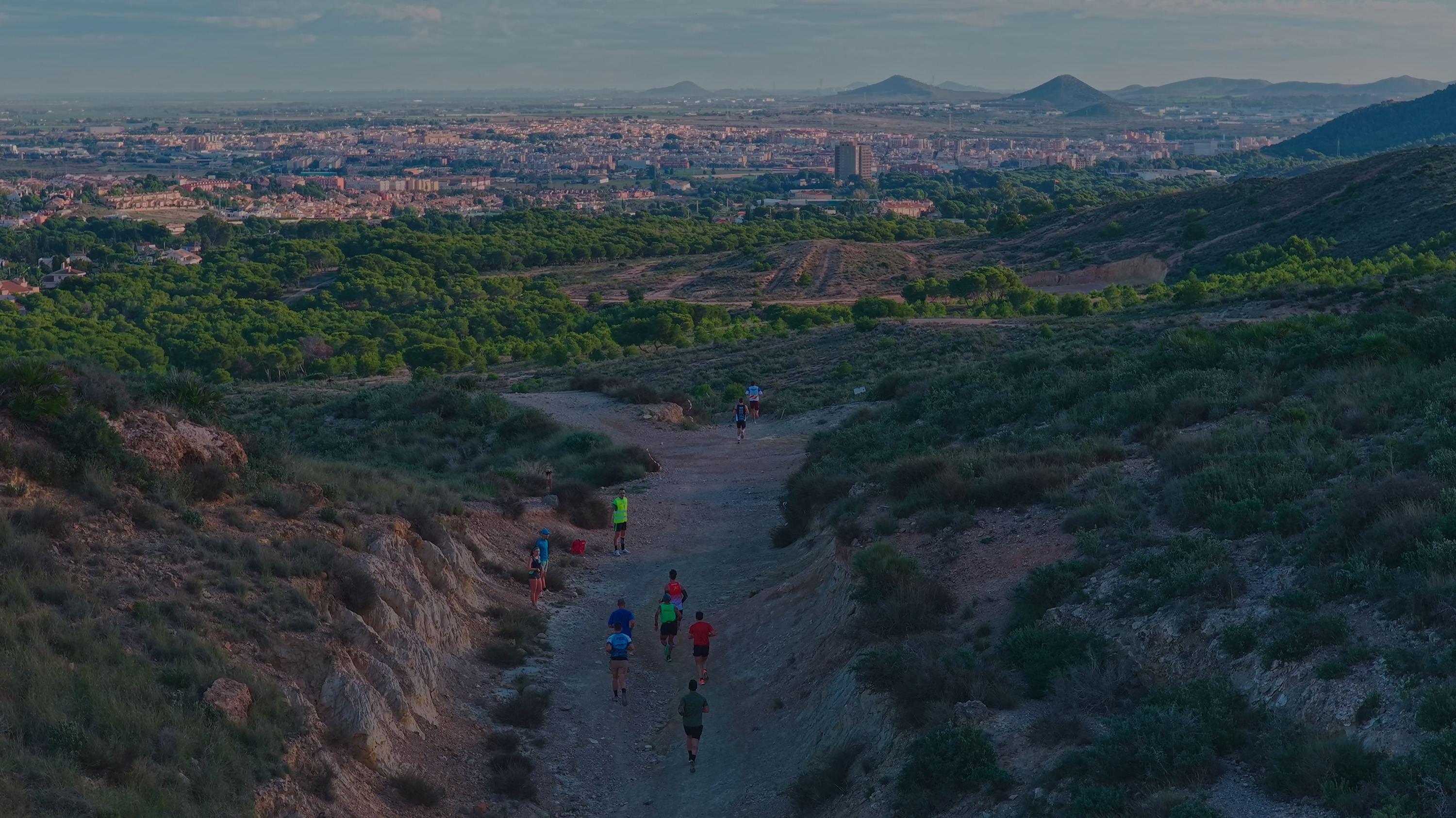 Runners on a trail with city and mountain views. Perfect Taiga: Corporativa for outdoor enthusiasts.