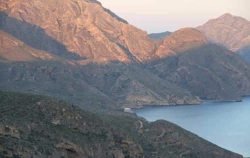 un hombre con una mochila y un sombrero se para en un acantilado mirando al océano