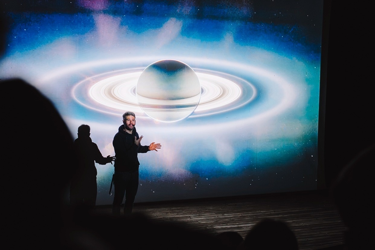 Ponente en sala de conferencias de hotel con pantalla gigante de espacio y planeta para eventos.