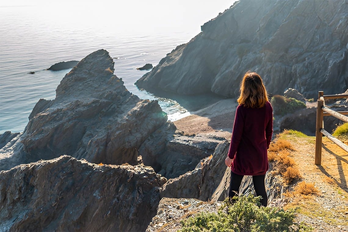 una mulher está de pé em um penhasco com vista para o oceano